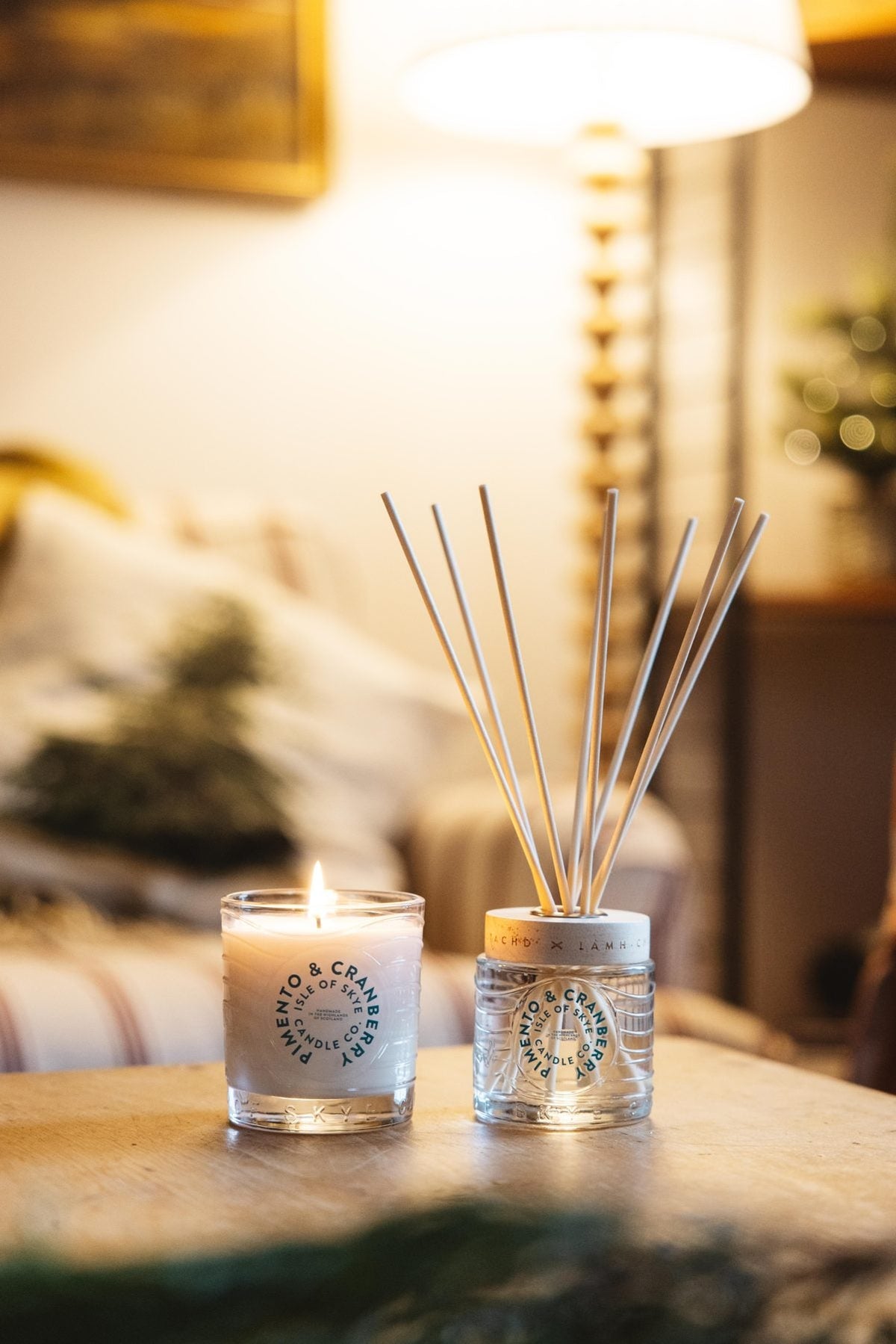 Pimento and Cranberry reed diffuser and candle on a wooden table in a warmly lit living room