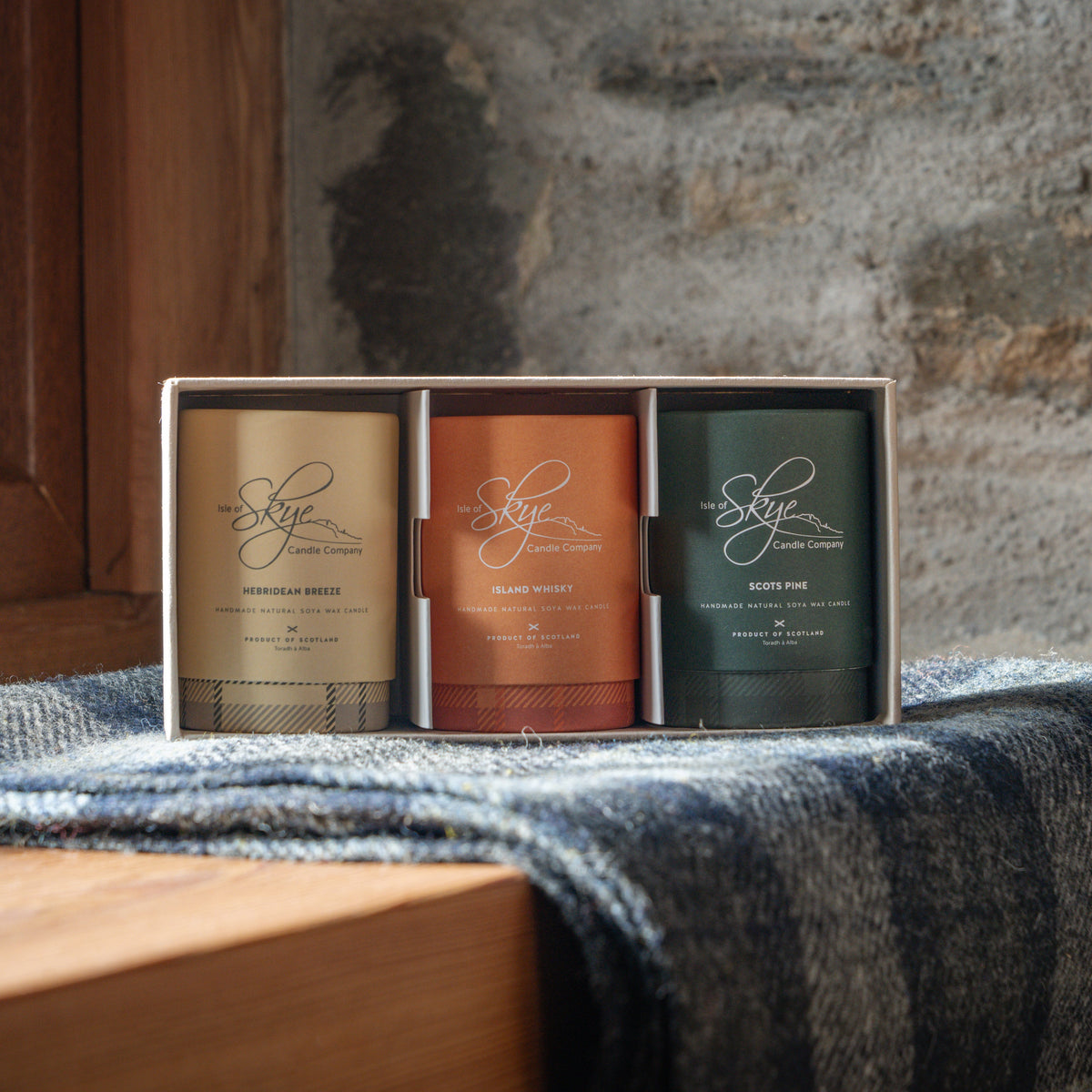 Three mini candles form the Isle of Skye Candle company and pictured on a woollen blanket on the windowsill in gift box.
